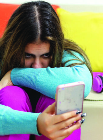 A depressed teenager checking at the mobile phone sitting in her room