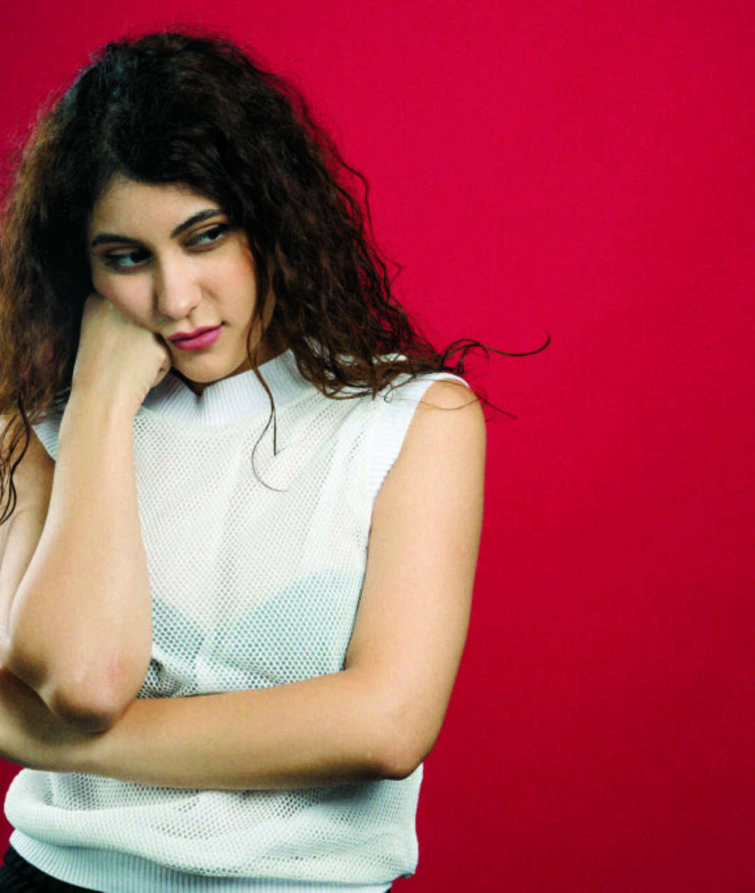 Young curly woman touching gently her face with raised hand on red background