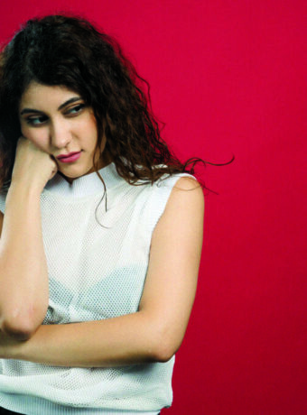 Young curly woman touching gently her face with raised hand on red background